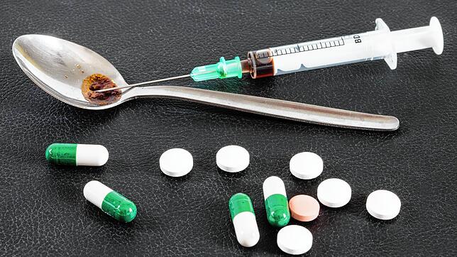 Unser Symbolbild zeigt verschiedene Drogen, die auf einem Tisch liegen. Hinten ist eine Spritze zu sehen. Damit wird meist Heroin ...