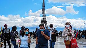 Passanten tragen am Platz Trocadero in der Nähe des Eiffelturms Mundschutze und Gesichtsmasken.