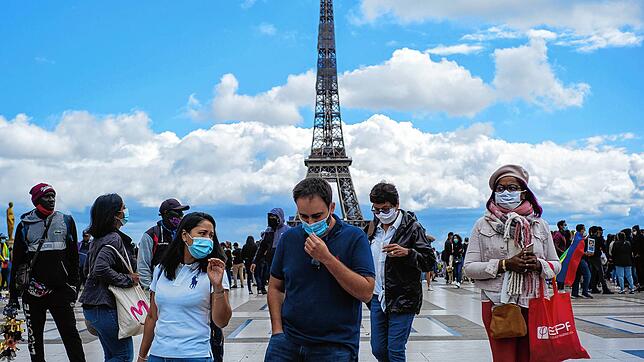 Passanten tragen am Platz Trocadero in der Nähe des Eiffelturms Mundschutze und Gesichtsmasken.
