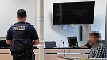 Der 33-Jährige auf der Anklagebank. Ein Justizbeamter hat sich im Gerichtssaal vor ihm positioniert.