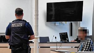 Der 33-Jährige auf der Anklagebank. Ein Justizbeamter hat sich im Gerichtssaal vor ihm positioniert.