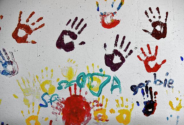 Bunte Powerkids-Hände an einer Wand.