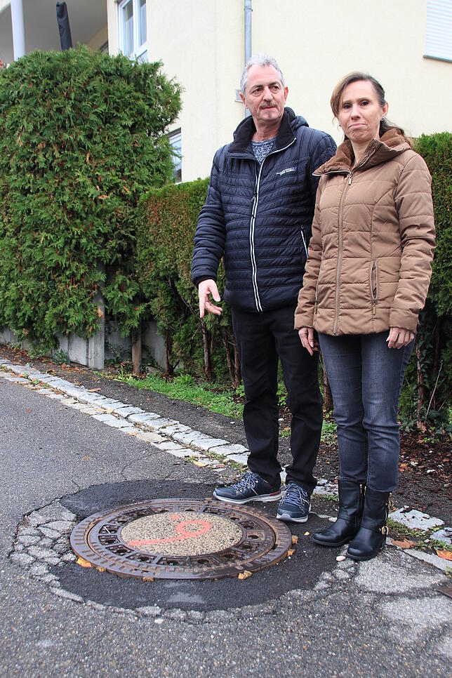 Maria Karrer und Jens Frömken leiden unter einem losen Schachtdeckel, der scheppert, wenn jemand mit seinem Auto drüberfährt.