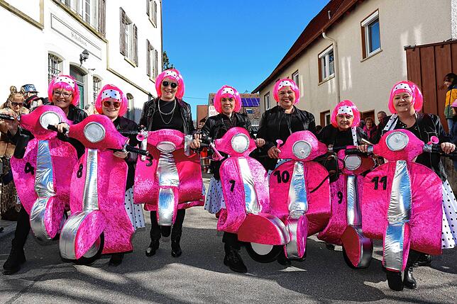 Fantasievolle Verkleidungen prägen das Bild. Unter dem Motto „Flotte Vespa“ sind die Rosenmontagsfrauen mit pinken Vespa-Rollern dabei.