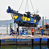 Der Bohrer, den der Autokran vorsichtig auf das zusammengebaute Ponton-Floß hinab lässt, wiegt rund 14 Tonnen. Das Boot im Hintergrund ...