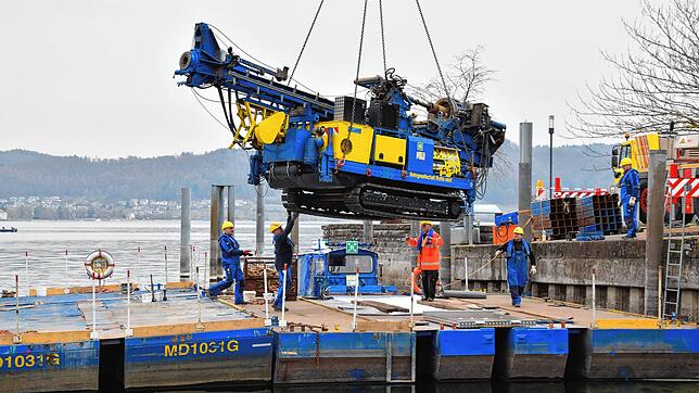 Der Bohrer, den der Autokran vorsichtig auf das zusammengebaute Ponton-Floß hinab lässt, wiegt rund 14 Tonnen. Das Boot im Hintergrund ...
