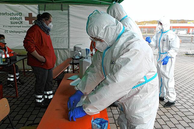 Die DRK-Mitglieder bereiten die Teststation vor. Vorgeschrieben sind Overall, Schutzbrille, medizinische Maske und Handschuhe.
