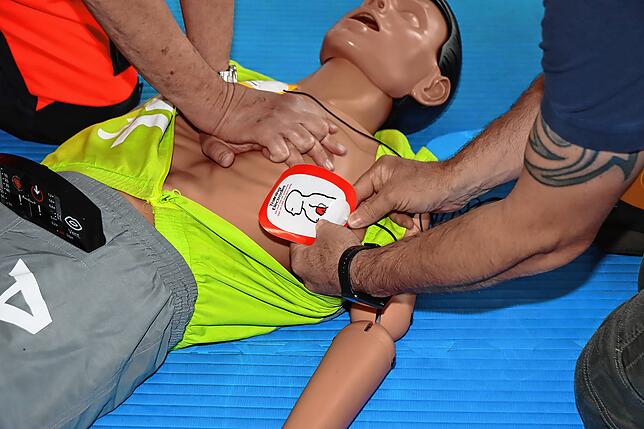 Ein Ersthelfer bringt die Elektroden des Defibrillationsgerätes am Patienten an.