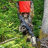 Gut getarnt und zur besseren Erkennung fürs Foto rot beflaggt. Ein getranter Schütze kauert im Weißwald bei Tannheim im Aoril 2021 unter ...