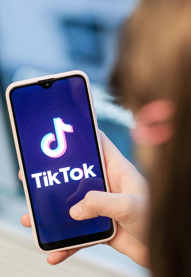 Ein Mädchen hält ihr Smartphone in den Händen, auf dem sie ein Foto der Kurzvideo-App TikTok geöffnet hat. Die App ist vor allem bei ...