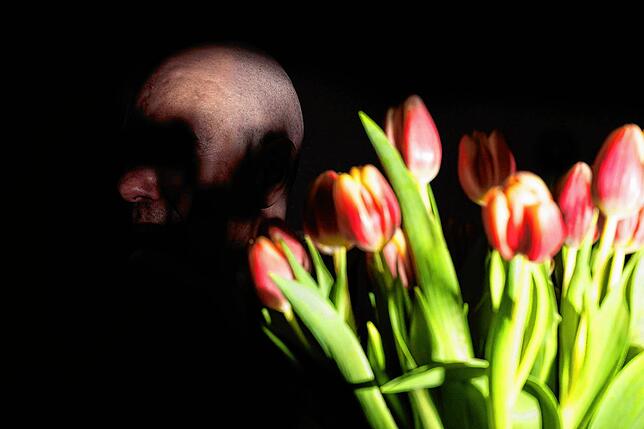Jochen sitzt hinter einem Tulpenstrauß an seinem Tisch im Wohnzimmer. Er möchte – genau wie die anderen – unerkannt bleiben.