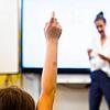 Ein Schüler meldet sich, während eine Lehrerin vor einer digitalen Schultafel steht.