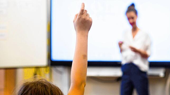 Ein Schüler meldet sich, während eine Lehrerin vor einer digitalen Schultafel steht.