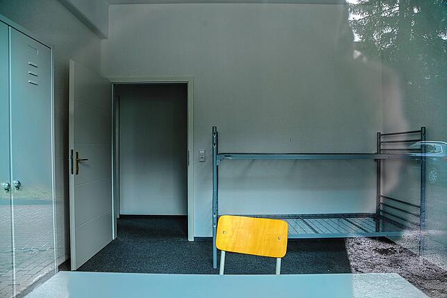 Blick durchs Fenster in einen der Räume mit Stockbett, Tisch und Stuhl.