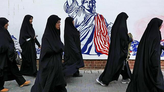 Die Teilnehmerinnen einer Trauerzeremonie für den getöteten General Soleimani gehen auf ihrem Heimweg an der satirischen Zeichnung einer ...