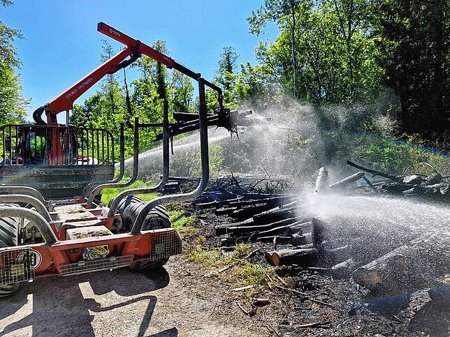 Der Förster hilft mit einem Traktor samt Rücke-Anhänger, den Haufen auseinanderzuziehen, um das Holz besser löschen zu können.