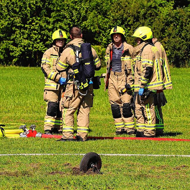 Vor den vier Feuerwehrleuten steckt deutlich sichtbar ein Rad des Ultraleichtflugzeugs in der Landebahn des Konstanzer Flugplatzes.