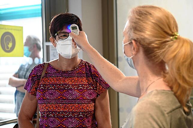 Melanie Reinl misst bei einer Impfteilnehmerin beim Eintritt zur Impfstation die Körpertemperatur mit dem elektronischen Thermometer.