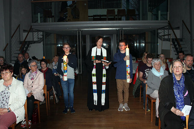 Pfarrerin Gabriele Remane und zwei Konfirmanden bringen die Osterkerze und die Gebetskerze für den Kindergottesdienst zum Altar.