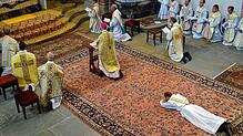 Weihekandidat Wolfgang Dichgans, noch im Gewand des Diakons, liegt ausgestreckt am Boden im Chorraum der Basilika Birnau.