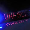 Das Blaulicht auf einem Fahrzeug der Polizei leuchtet in der Dunkelheit, während auf dem Display der Hinweis „Unfall“ zu lesen ist.