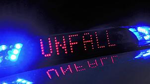 Das Blaulicht auf einem Fahrzeug der Polizei leuchtet in der Dunkelheit, während auf dem Display der Hinweis „Unfall“ zu lesen ist.