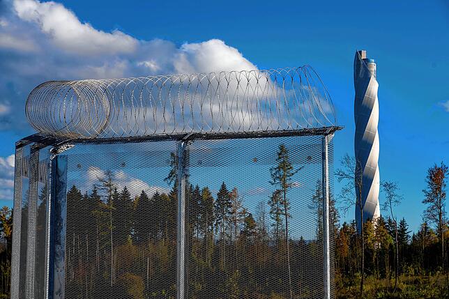 Am zukünftigen Knast schlängelt sich Stacheldraht in die Breite, der Aufzug-Testturm im Hintergrund reckt sich in die Höhe.