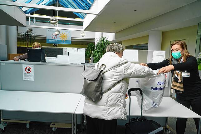 Eine Frau gibt Kleidung für ihren Mann im Eingangsbereich ab. Die Mitarbeiterin verstaut diese in einer Tüte. Besuchen darf die Dame ...