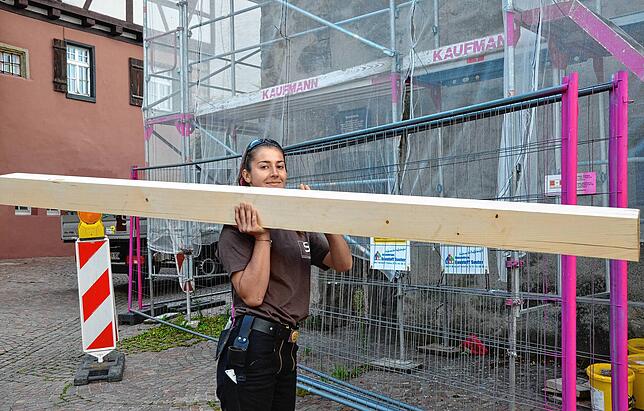 Franca Schwarz, Zimmerer-Auszubildende im ersten Lehrjahr bei Holzbau Schmäh, trägt einen Dachbalken, der einen feucht gewordenen alten ...