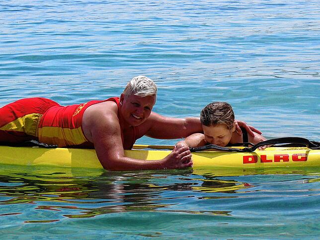 Sybille Rinn und ihre Tochter Svea zeigen, wie eine Rettungsschwimmerin eine erschöpfte Schwimmerin aufs Rettungsbrett hebt.