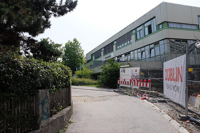 Auch die aktuelle Aufnahme zeigt eine Frontalsicht auf die Schule mit dem Haupteingang. Im Zuge des Schulcampus entstand die Baustelle.