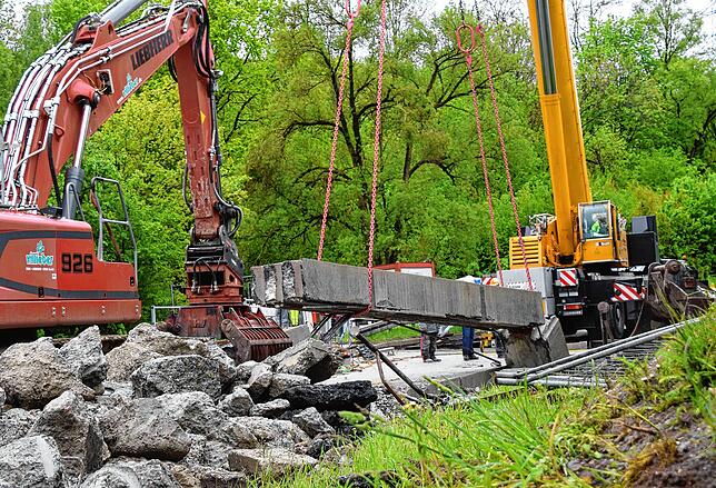 Ein Bagger mit verschiedenen Aufsätzen und der Autokran sind im Einsatz, um die Brücke Stück für Stück zu entfernen.