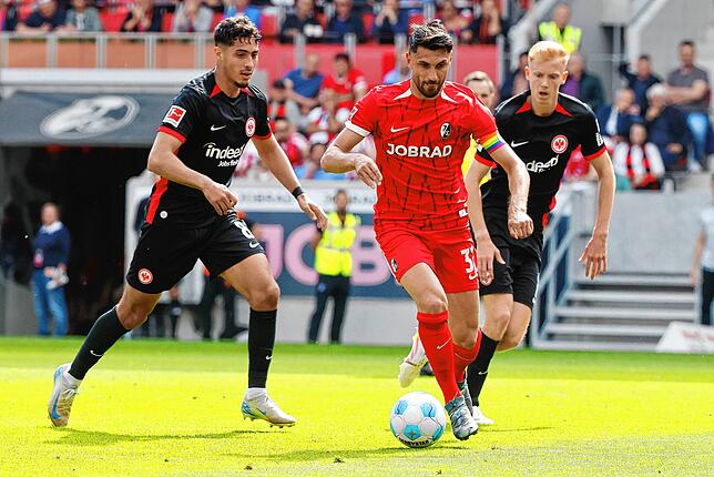 Frankfurts Fares Chaibi und Freiburgs Vincenzo Grifo (m) im Kampf um den Ball während dahinter Frankfurts Hugo Larsson zu sehen ist.