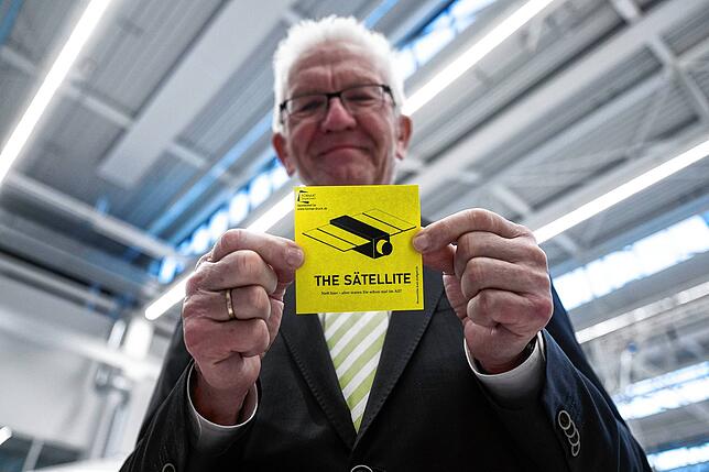 Winfried Kretschmann, Ministerpräsident von Baden-Württemberg, zeigt während eines Besuchs der Universität Stuttgart einen Aufkleber mit ...