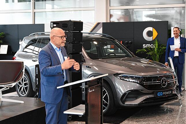 Landesverkehrsminister Winfried Hermann (Grüne) zu Gast im Autohaus – vor der Kulisse eines Elektroautos. Im Hintergrund Volker ...