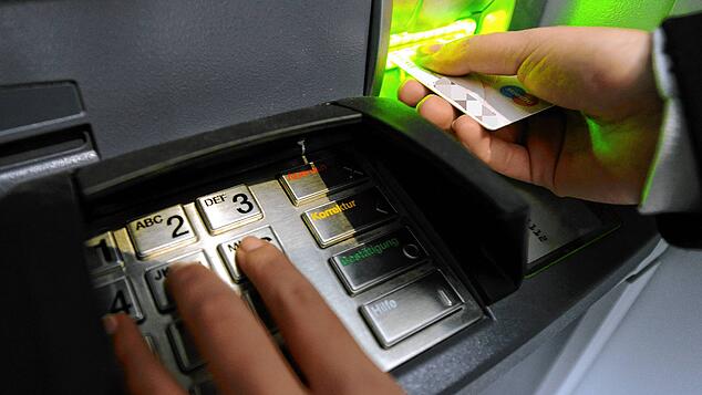 Jemand tippt die PIN der EC-Karte an der Tastatur eines Geldautomaten einer Bank ein.