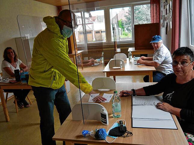 Wahlhelferin Melitta Veser nimmt den Wahlschein von Guido Keller entgegen. Im Hintergrund sind die beiden Wahlkämpfer Anja Schädler und ...