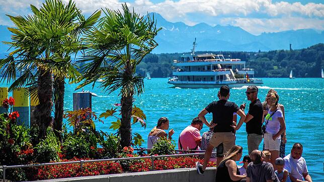 Touristen blicken am Überlinger Hafen auf die Fähre und den türkisblauen See.