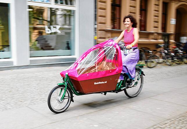 Eine Frau fährt mit einem Lasten-Fahrrad auf einem Radweg.