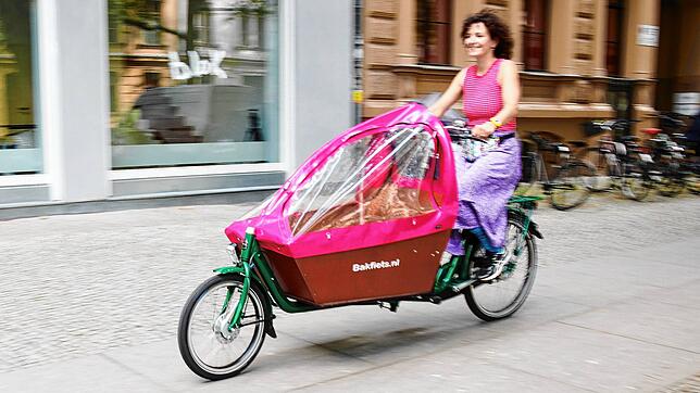 Eine Frau fährt mit einem Lasten-Fahrrad auf einem Radweg.