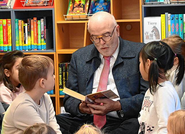 Bürgermeister Rainer Rainer Stolz sitzt im Schneidersitz zwischen Kindern und liest vor.