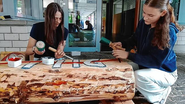 Emily Schlageter und Laura Schrempp bearbeiten mit Schnitzmesser und Hammer einen Baumstamm. Foto: Christoph Schennen