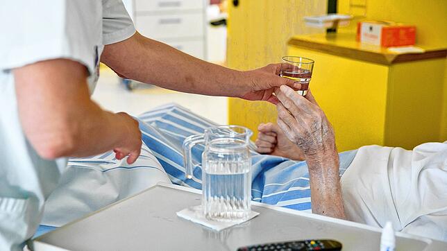 Eine Krankenpflegerin reicht einem Patienten in der Onkologie in einem Klinikum ein Glas Wasser.