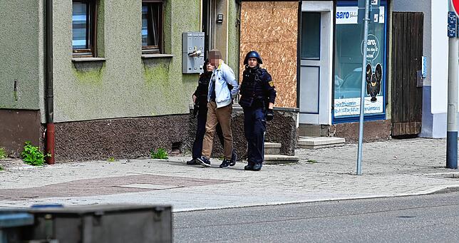 Zwei schwer bewaffnete und mit Spezialausrüstung geschützte Polizisten bringen den Mann aus einem Haus in der Schützenstraße.