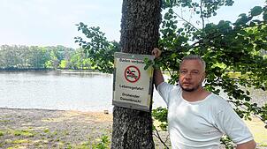 Andreas Preiser steht neben dem Hinweisschild, dass das Baden im Schlüchtsee derzeit verboten ist.