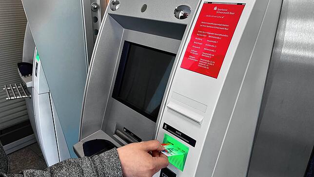 Blick über die Schulter einer Bankkundin an einem Geldautomaten (Symbolbild). Die Polizei warnt vor einer neuen Betrugsmasche, bei der ...