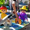 Die Stadtverwaltung möchte die Kita-Gebühren für Eltern, symbolisch dargestellt durch die Playmobil-Figuren vor dem katholischen ...