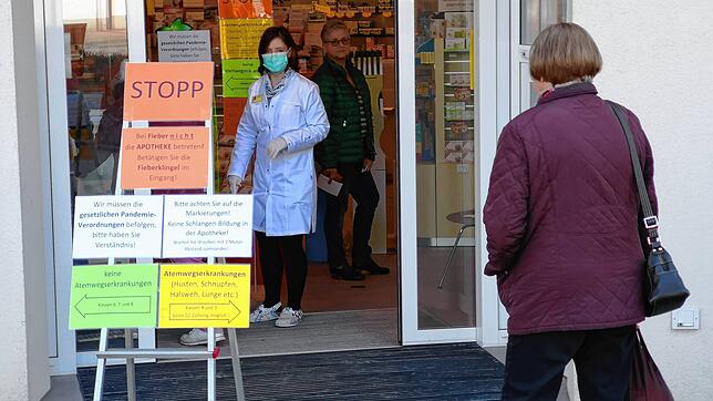 Eine Mitarbeiterin der Einhorn-Apotheke steht im Eingangsbereich und informiert die Kunden über Coronavirus-bedingte Sicherheitshinweise.