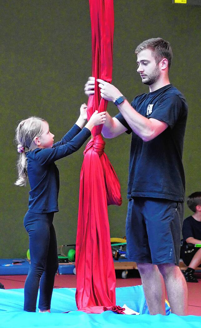 Zirkustrainer Paul hilft auf einer Zirkusfreizeit der jungen Artistin Miriam (10) mit dem Vertikaltuch.