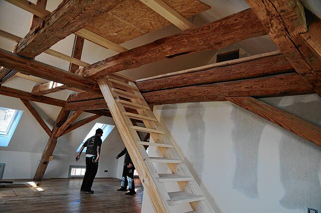 Die Dachwohnung im Anbau zeigt offenes Gebälk, eine Treppe führt auf die Galerie, die Balken zeigen Geschichte.